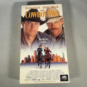 Könnte beinhalten: Eine VHS-Kassette für den Film "The Cowboy Way" mit Woody Harrelson und Kiefer Sutherland. Das Cover zeigt die Schauspieler und Cowboys auf Pferden mit einer Skyline.