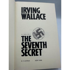 May include: Open book with the title "The Seventh Secret" by Irving Wallace. The book cover is cream-colored with black text. A circular graphic with puzzle pieces is on the cover. Published by E.P. Dutton, New York.