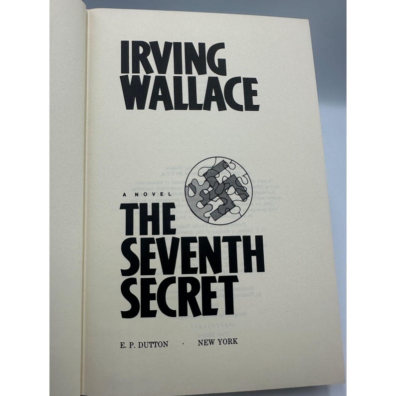 May include: Open book with the title "The Seventh Secret" by Irving Wallace. The book cover is cream-colored with black text. A circular graphic with puzzle pieces is on the cover. Published by E.P. Dutton, New York.