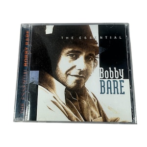 May include: A compact disc case featuring a portrait of Bobby Bare. The album cover has the text "THE ESSENTIAL" at the top and "Bobby BARE" in a bold font on the right side. The spine reads "THE ESSENTIAL BOBBY BARE".