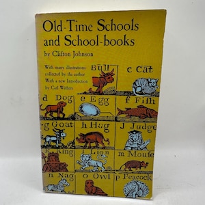 Puede incluir: Un libro antiguo titulado "Old-Time Schools and School-books" de Clifton Johnson. La portada es amarilla con texto negro e ilustraciones de animales y objetos, incluyendo un toro, gato, perro, huevo, pez, cabra, cerdo, juez, rey, león, ratón, caballo, búho y pavo real.