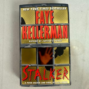 May include: A book cover for "Stalker" by Faye Kellerman. The cover features a window design with the author's name in red, the title in red, and a hand silhouette. The book is a Peter Decker and Rina Lazarus novel.