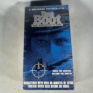 May include: Sealed VHS tape of the film "Das Boot: The Director's Cut". The cover is predominantly blue, featuring a submarine and a man's face. Text includes "A Wolfgang Petersen Film" and "When the Hunters Become the Hunted."