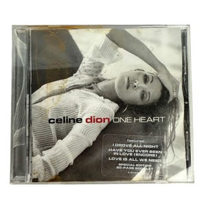 Puede incluir: Una caja de CD con el álbum "One Heart" de Celine Dion. La portada presenta una foto en blanco y negro de Celine Dion. El título del álbum y el nombre del artista están impresos en la portada. La caja también incluye una pegatina con los títulos de las canciones.