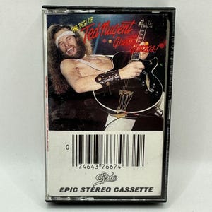 Pode incluir: Uma fita cassete vintage com o álbum "The Best of Ted Nugent - Great Gonzos!". A capa mostra um homem tocando uma guitarra elétrica preta. A fita é rotulada como "Epic Stereo Cassette".