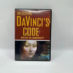 May include: DVD case with the title "Unlocking DaVinci's Code" in yellow letters on a brown background. The bottom half features a portrait of a woman. The text "Mystery or Conspiracy?" is below the title.