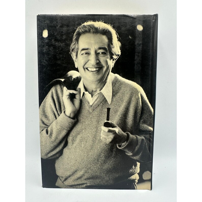 May include: A sepia-toned image of a smiling person holding a pipe and a jacket over their shoulder. The person is wearing a light-colored sweater over a collared shirt. The background is dark.
