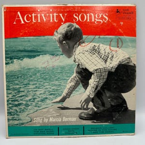 Può includere: Una copertina di disco in vinile vintage intitolata Activity Songs di Tom Thumb Records. La copertina mostra un bambino con una camicia a quadri e pantaloni scuri accovacciato vicino all'oceano. Il testo include titoli come I'm Not Small e The Bee Song.