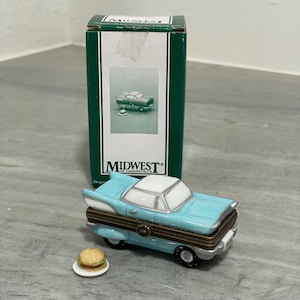 May include: A light blue vintage car-shaped trinket box with a white roof and brown accents. The box sits in front of a green box with the "Midwest of Cannon Falls" logo. A small ceramic burger is next to the car.
