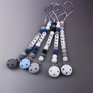 Peut inclure: Plusieurs attaches-sucettes pour bébés de différentes couleurs, dont le gris, le bleu et le blanc. Chaque attache-sucette comporte un nom épelé avec des perles de lettres blanches. Les attaches-sucettes ont un support de sucette rond en silicone et un clip en métal.