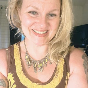 Puede incluir: Una mujer con cabello rubio lleva un top sin mangas de color marrón y amarillo con un collar plateado con detalles amarillos.