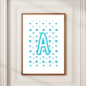 Könnte beinhalten: Ein weißer gerahmter Druck mit einem blauen Buchstaben A, umgeben von einem Muster aus blauen Herzen auf weißem Hintergrund.
