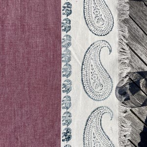 Può includere: Tessuto bordeaux con bordo bianco con motivo ripetuto di elefanti blu e grandi disegni paisley. Il bordo del tessuto ha una finitura sfrangiata. Il tessuto è probabilmente un oggetto decorativo, come una sciarpa o un runner da tavolo.
