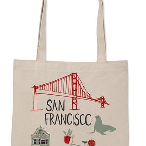 May include: A beige canvas tote bag with a red and white illustration of the Golden Gate Bridge, the text "SAN FRANCISCO", a green house, a bicycle with a basket and a pumpkin, and a grey seal. The bag has a white logo that says "CLAIRE PEARSON".