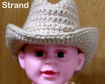 May include: A beige crocheted cowboy hat with the text "Easy Creations" on the brim. The hat is on a child's head.