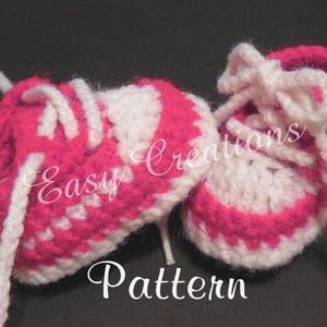 Peut inclure: Une paire de chaussons pour bébé en crochet rose et blanc avec des lacets blancs. Les chaussons sont en forme de baskets et ont une bordure blanche autour des bords. Le texte "Easy Creations Pattern" est visible sur l'image.