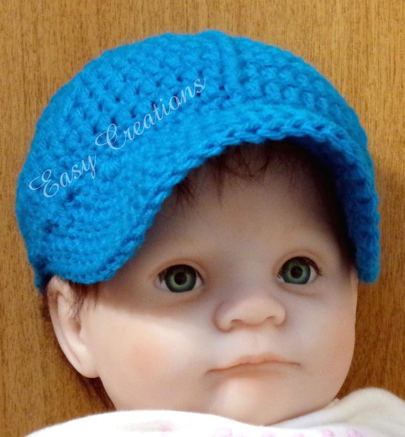 Puede incluir: Un beb&eacute; con un gorro de punto azul brillante con visera. El gorro tiene el texto "Easy Creations" bordado en un lateral.