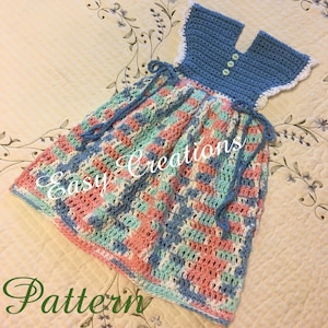 Könnte beinhalten: Ein gehäkeltes Geschirrtuch in Form eines Kleides mit einem blauen Oberteil und einem mehrfarbigen Rock. Der Rock ist aus rosa, blauem und weißem Garn gefertigt. Das Kleid hat einen weißen Häkelrand um den Ausschnitt und eine blaue Häkelschnur an der Taille. Das Geschirrtuch liegt auf einer weißen Oberfläche mit Blumenmuster. Der Text "Easy Creations Pattern" ist in der linken unteren Ecke des Bildes sichtbar.