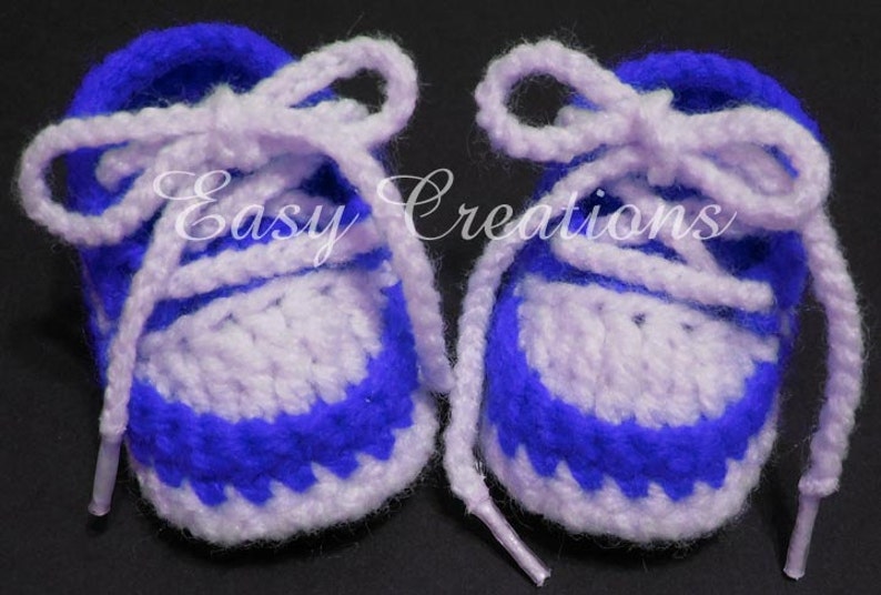 May include: A pair of crocheted baby booties in purple and white with white laces. The booties have a blue and white striped pattern.