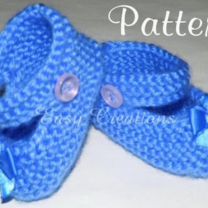 Op de afbeelding: Een paar blauwe gebreide babyschoentjes met witte knopen en blauwe satijnen strikjes. De schoentjes hebben een eenvoudig steekpatroon en zijn versierd met een parel op elk strikje.