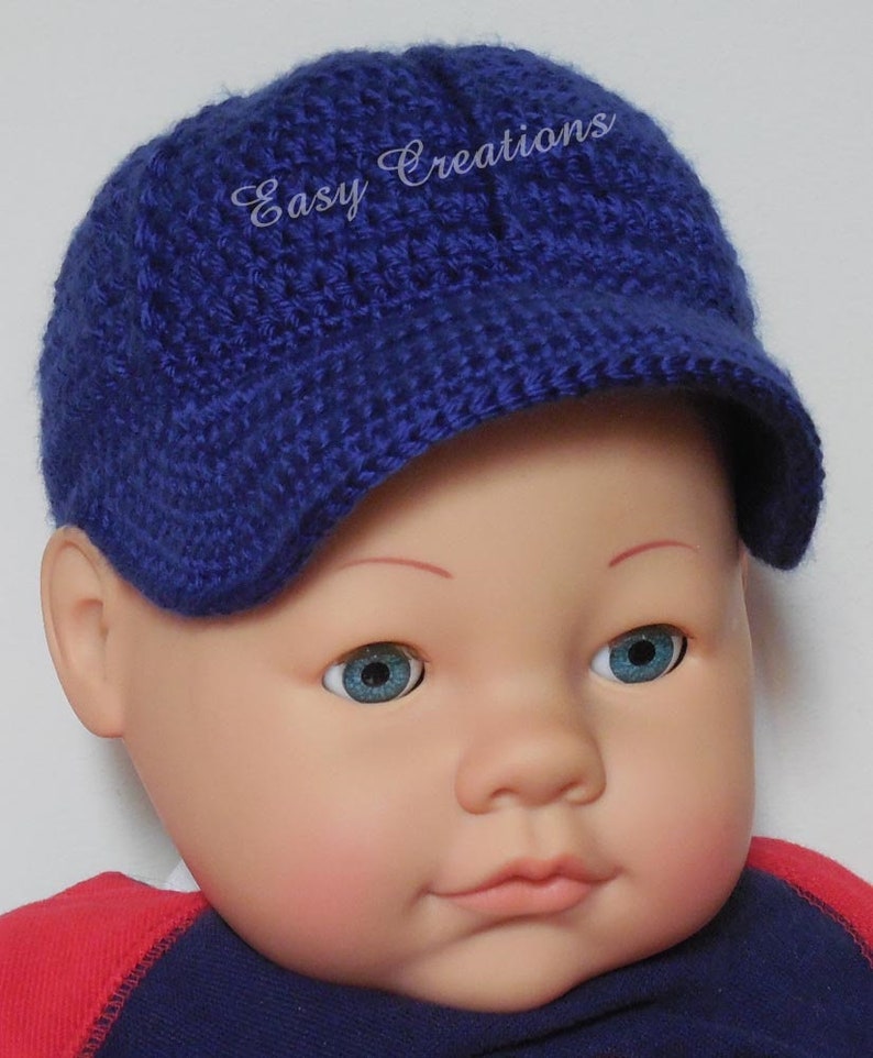 Puede incluir: Un gorro de beb&eacute; de crochet azul con visera y el texto "Easy Creations" bordado en la parte delantera.