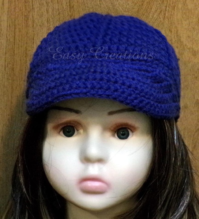 Puede incluir: Un gorro azul tejido a crochet con visera. El gorro tiene un dise&ntilde;o texturizado y las palabras "Easy Creations" est&aacute;n bordadas en la parte delantera.