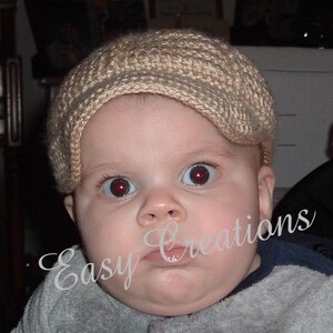 Puede incluir: Un beb&eacute; con un gorro de punto beige con visera. El gorro est&aacute; hecho con un patr&oacute;n de punto sencillo y tiene un aspecto suave y texturizado.