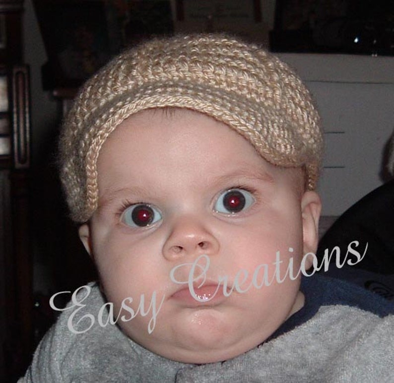Puede incluir: Un beb&eacute; con un gorro de punto beige con visera. El gorro est&aacute; hecho con un patr&oacute;n de punto sencillo y tiene un aspecto suave y texturizado.