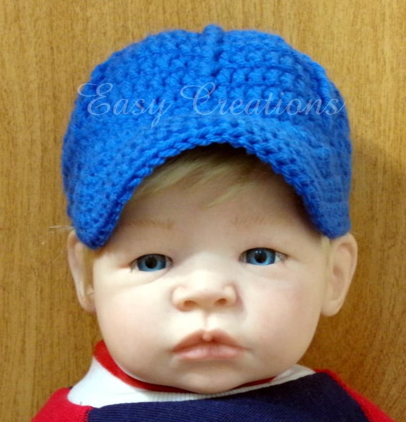 Puede incluir: Un beb&eacute; con una gorra de b&eacute;isbol de crochet azul. La gorra tiene visera y est&aacute; hecha con un punto texturizado.