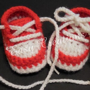 May include: A pair of red and white crocheted baby booties with white laces. The booties have a simple design and are perfect for a newborn.