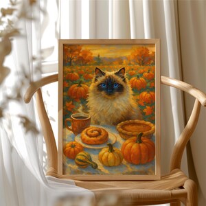 May include: A framed print of a cat with blue eyes, surrounded by pumpkins and autumn foliage. A table is set with a cup of coffee, a pastry, and a pie. The artwork is displayed on a wooden chair.