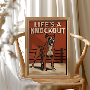 May include: A framed print with a boxer dog standing in a boxing ring. The text "LIFE'S A KNOCKOUT" is printed in bold white letters on a red background.