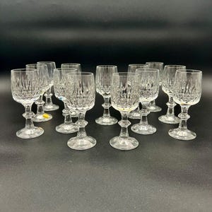 May include: A collection of clear crystal wine glasses with a textured, vertical pattern. The glasses have a stemmed base and a rounded bowl. The glasses are arranged on a dark surface.