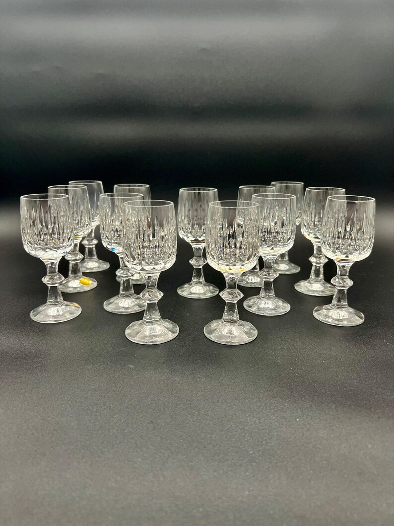 May include: A collection of clear crystal wine glasses with a textured, vertical pattern. The glasses have a stemmed base and a rounded bowl. The glasses are arranged on a dark surface.