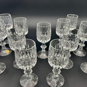 May include: A collection of clear crystal wine glasses with a cut glass design. The glasses have a faceted stem and a round base. The glasses are arranged on a dark surface.