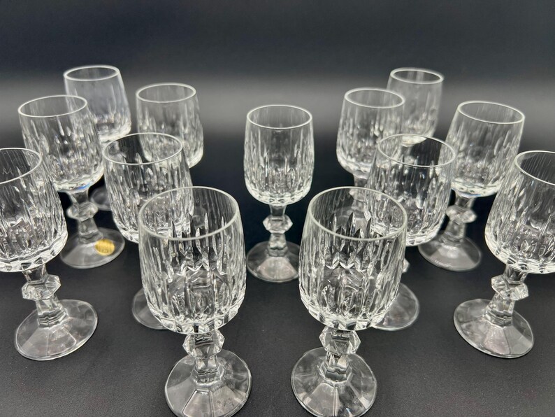 May include: A collection of clear crystal wine glasses with a cut glass design. The glasses have a faceted stem and a round base. The glasses are arranged on a dark surface.
