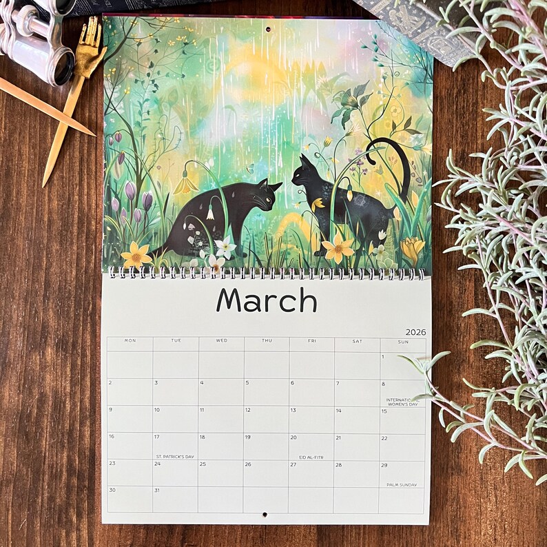 May include: A 2026 wall calendar featuring a watercolor illustration of two black cats in a garden setting. The word "March" is displayed prominently. The calendar includes a monthly view with dates and days of the week.