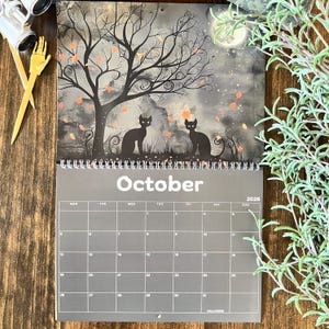 May include: A Halloween-themed calendar for October 2026, featuring a spooky illustration of two black cats under a bare tree with orange leaves. The background is a dark, cloudy sky with a full moon. The word "October" is printed in white.