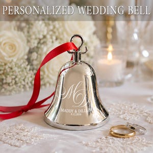 May include: A polished silver-toned metal wedding bell featuring a red ribbon tied to the top loop. The bell is engraved with the monogram MD, the names MADDY & DILLON, and the date 9.12.2026. The text PERSONALIZED WEDDING BELL appears at the top.