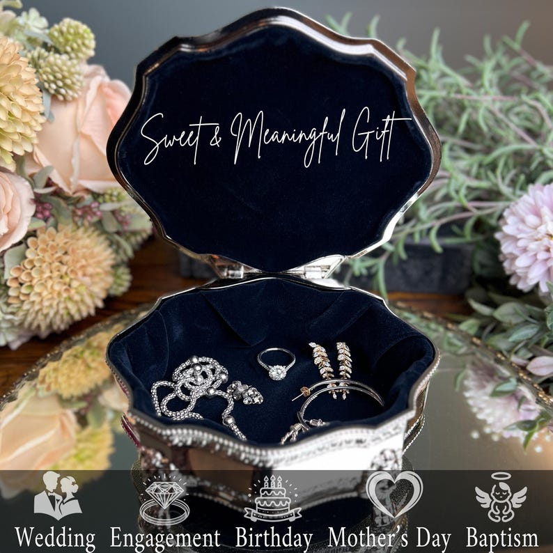 May include: A silver-toned metal jewelry box with a scalloped edge and dark blue velvet lining. The interior lid features the white text Sweet & Meaningful Gift. Inside, a silver chain, a ring, and hoop earrings are displayed on the velvet.