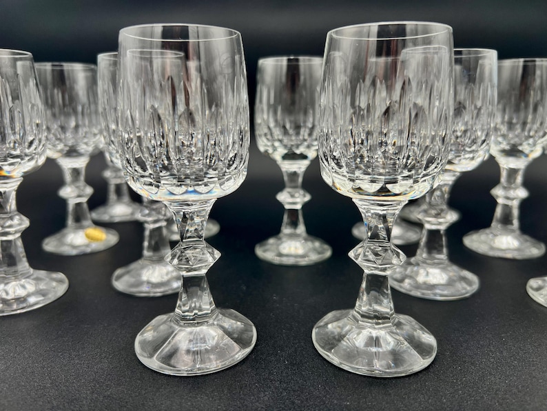 May include: A collection of clear crystal wine glasses. The glasses have a detailed, textured pattern on the bowl and a faceted stem. The glasses are arranged on a dark surface, showcasing their elegant design. Ideal for serving wine.