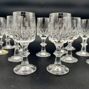 May include: A collection of clear crystal wine glasses. Each glass features a detailed, textured pattern on the bowl and a decorative stem. The glasses are arranged on a dark surface, showcasing their elegant design.