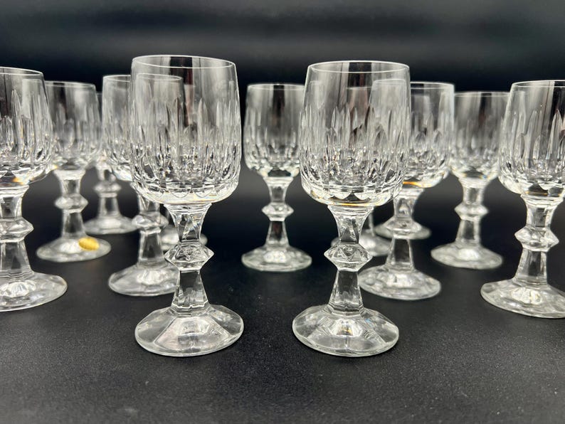 May include: A collection of clear crystal wine glasses. Each glass features a detailed, textured pattern on the bowl and a decorative stem. The glasses are arranged on a dark surface, showcasing their elegant design.