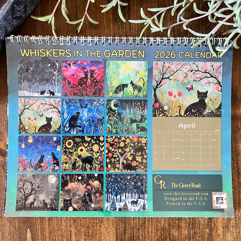 May include: A spiral-bound 2026 calendar titled "Whiskers in the Garden." The calendar features monthly illustrations of black cats in various garden settings. The April page is visible, with a black cat under a flowering tree. The Clover Road logo is at the bottom.