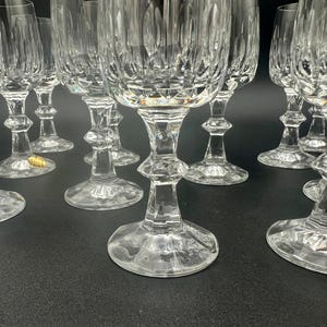 May include: A collection of clear crystal wine glasses. The glasses have a detailed, textured design on the bowl and stem. The stems have a decorative, bulbous shape. The glasses are arranged on a dark surface.