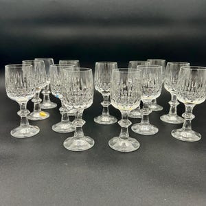 May include: A collection of clear crystal wine glasses. Each glass features a textured, vertical pattern on the bowl, a detailed stem, and a round base. The glasses are arranged on a dark surface.