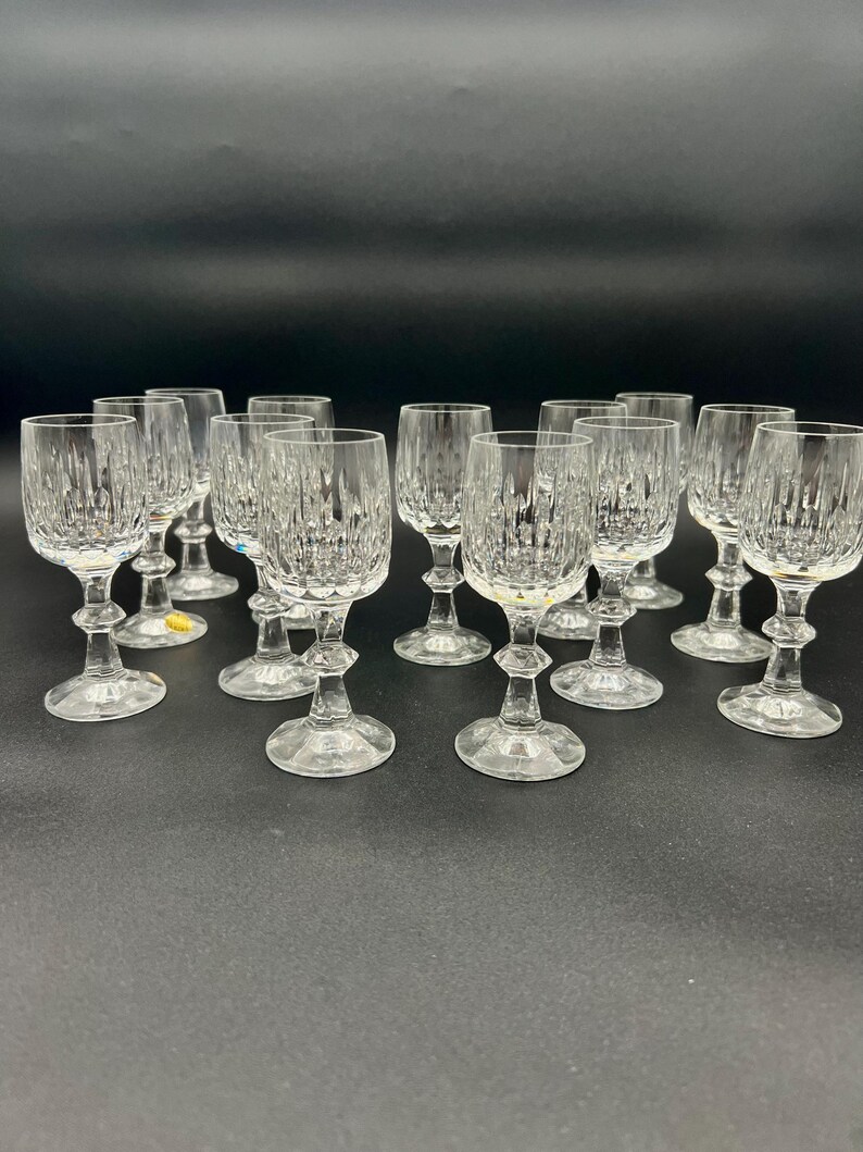 May include: A collection of clear crystal wine glasses. Each glass features a textured, vertical pattern on the bowl, a detailed stem, and a round base. The glasses are arranged on a dark surface.