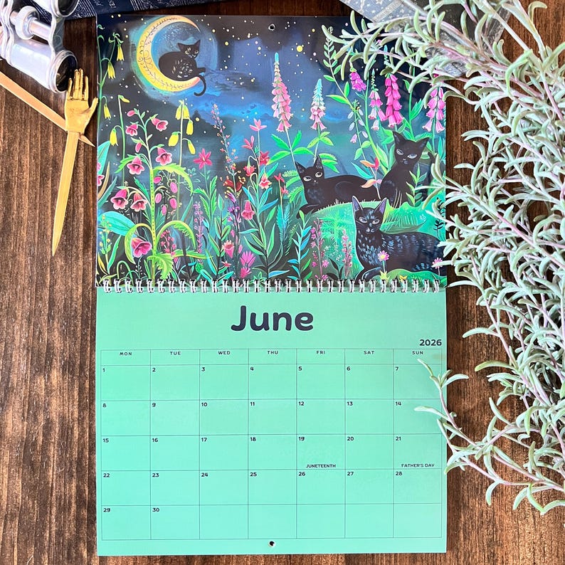 May include: A 2026 wall calendar featuring a whimsical illustration of black cats in a moonlit garden. The calendar page for June is displayed, with a green background and dates. The artwork includes vibrant colors and floral elements.