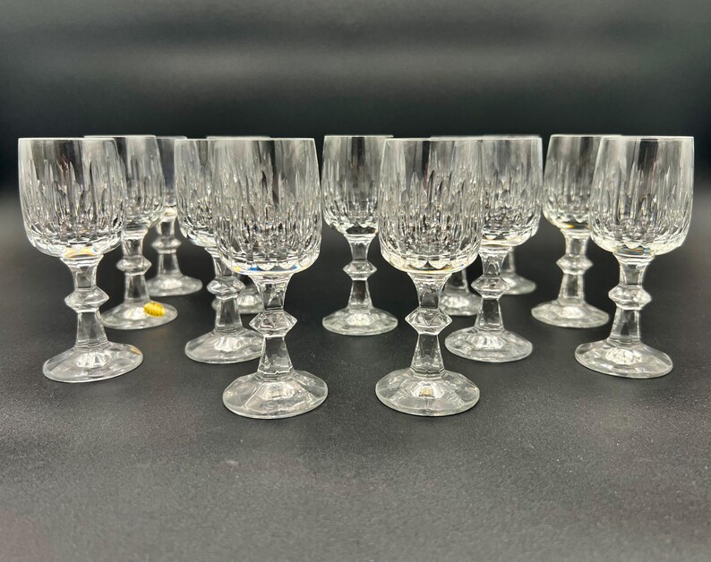 May include: A collection of clear crystal wine glasses. Each glass features a textured, vertical pattern on the bowl, a decorative stem, and a round base. The glasses are arranged on a dark surface.