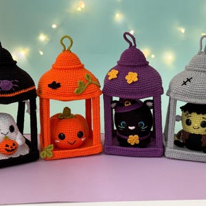 Pode incluir: Quatro decorações de crochê em forma de lanterna com personagens de Halloween. A lanterna preta contém um fantasma branco com uma abóbora, a laranja uma abóbora, a roxa um gato preto e a cinza um monstro de pele verde.
